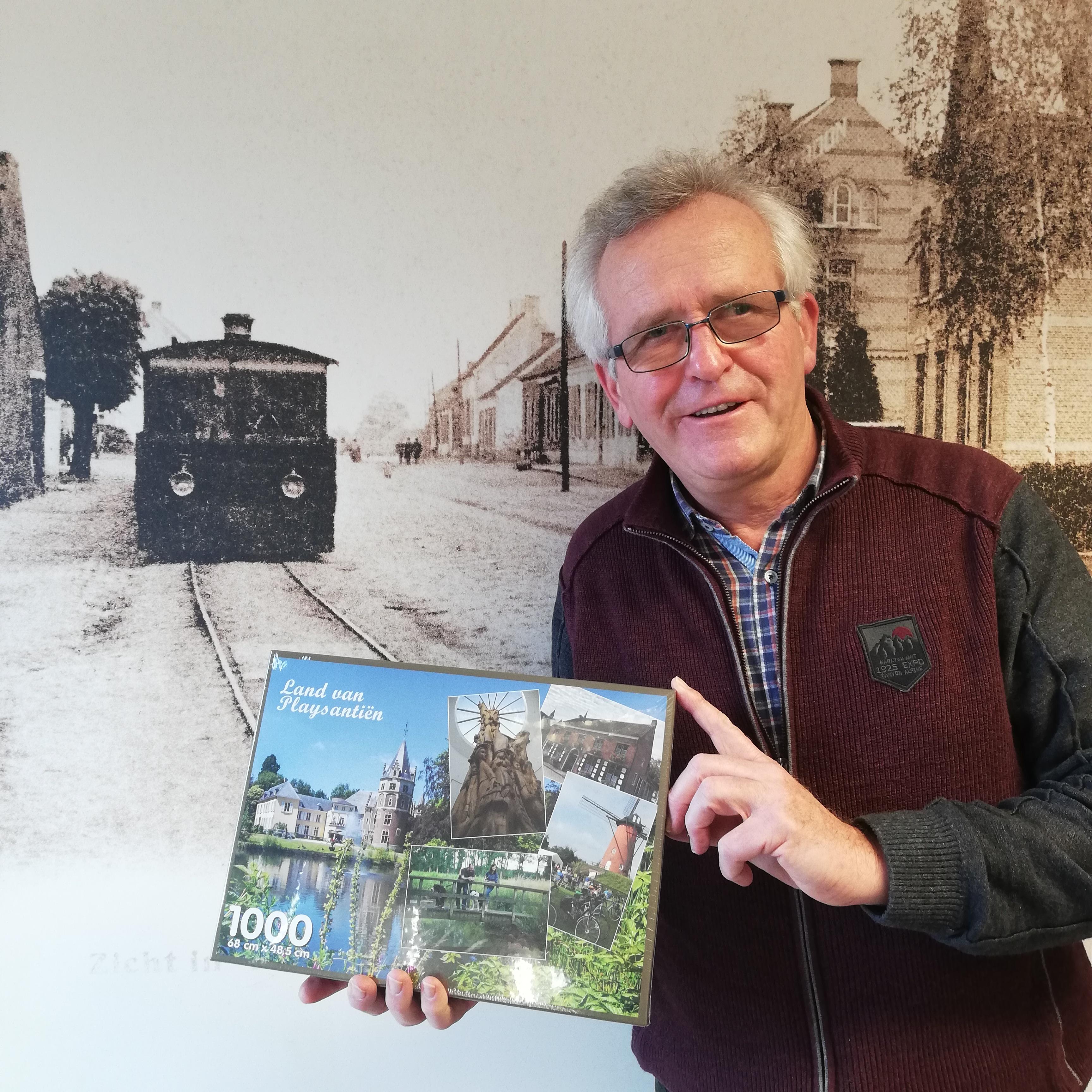 Jan Q. die het idee van de puzzel naar voor schoof, poseert met de puzzel van Land van Playsantiën voor een afbeelding van de stoomtram.